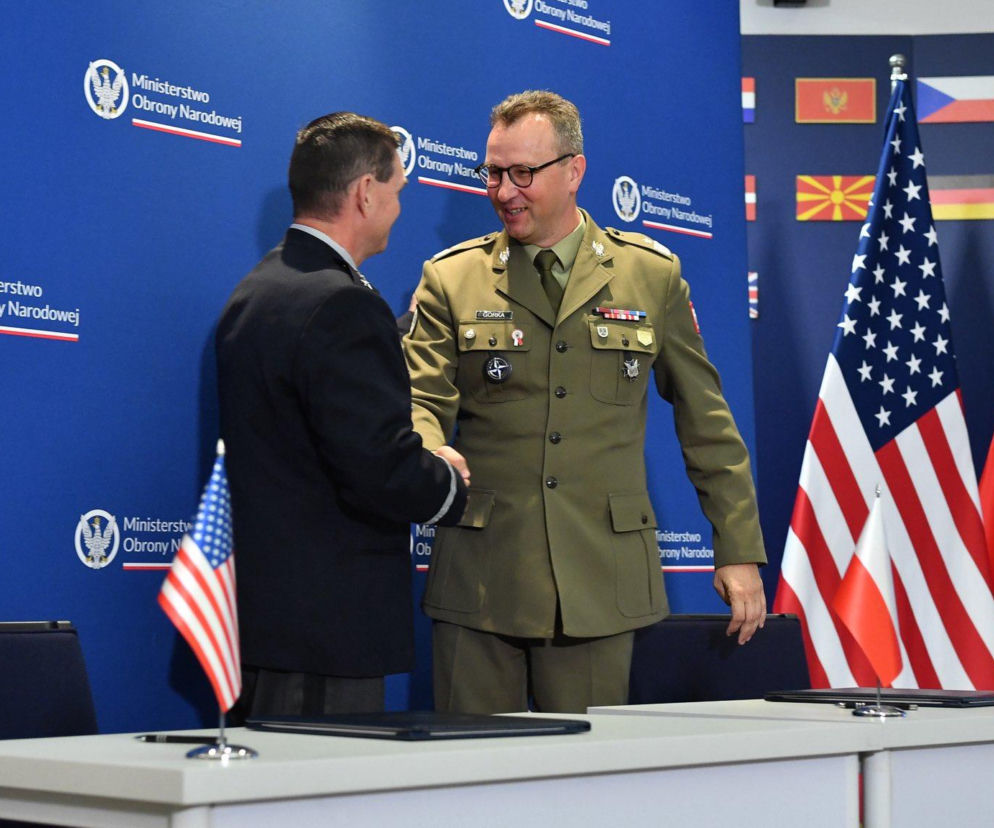 Uśmiechnięci oficerowie Polski i USA podają sobie dłonie nad dokumentami. O współpracy MON przeczytasz na SE Portal Obronny.