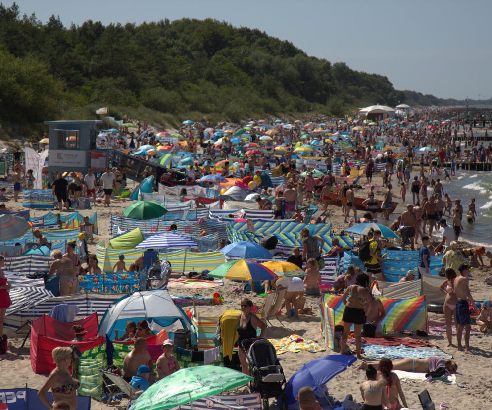 Tłum ludzi na słonecznej plaży pełnej parawanów. O ryzyku oparzeń słonecznych przeczytasz na Poradnik Zdrowie.
