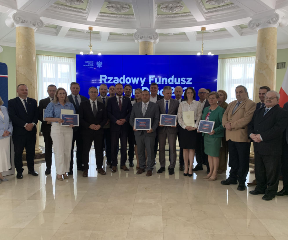 Uczestnicy uroczystości podpisania umów na dofinansowanie inwestycji drogowych w Lubelskiem, z wojewodą Krzysztofem Komorskim i samorządowcami, prezentują certyfikaty. Więcej o milionach na lubelskie drogi przeczytasz na naszym portalu.