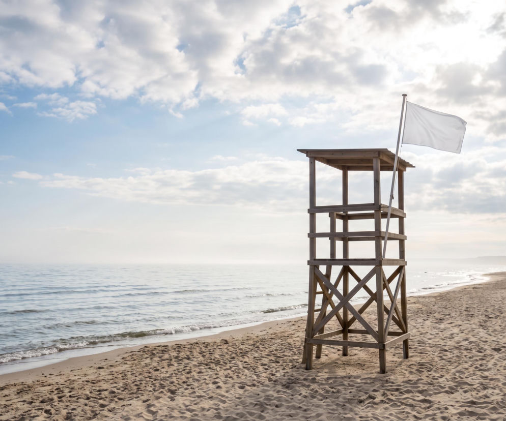 Drewniana wieża ratownicza z białą flagą na plaży w Chłopach. O bezpiecznej kąpieli przeczytasz na SE Szczecin.