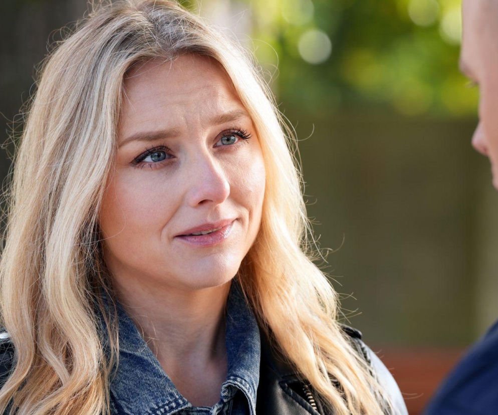 Kobieta o blond włosach, Grażyna (Kinga Suchan) z serialu Barwy szczęścia, w skórzanej kurtce i dżinsowej koszuli, spogląda w prawą stronę na niezidentyfikowanego mężczyznę. Jej twarz wyraża smutek i zamyślenie, co odzwierciedla trudną rozmowę o końcu związku, którą można przeczytać na Super Seriale.