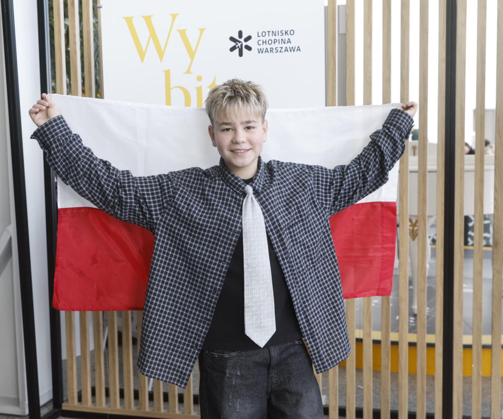 Uśmiechnięty Wiktor Sas trzyma polską flagę na Lotnisku Chopina. O finale Eurowizji Junior 2026 przeczytasz w VOX FM.