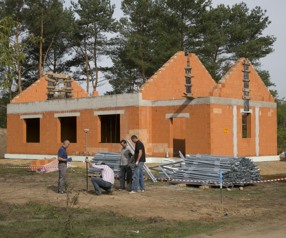 Czterej mężczyźni pracują na budowie domu w stanie surowym. O ukrytych kosztach w kosztorysie przeczytasz na Muratordom.