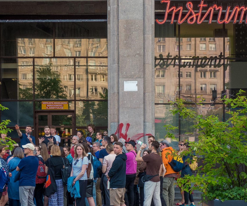 Grupa ludzi przed budynkiem z neonem Instrumenty na placu Konstytucji. O historii MDM przeczytasz na portalu Architektura.