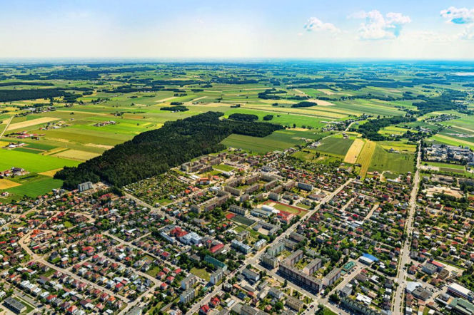 Lotniczy widok na miasto Mońki, otoczone zielonymi polami i lasami, ukazujący urbanizację wsi i malowniczą przyrodę Podlasia. O Wakacyjnym Starcie w Powiecie Monieckim przeczytasz więcej na naszym portalu.
