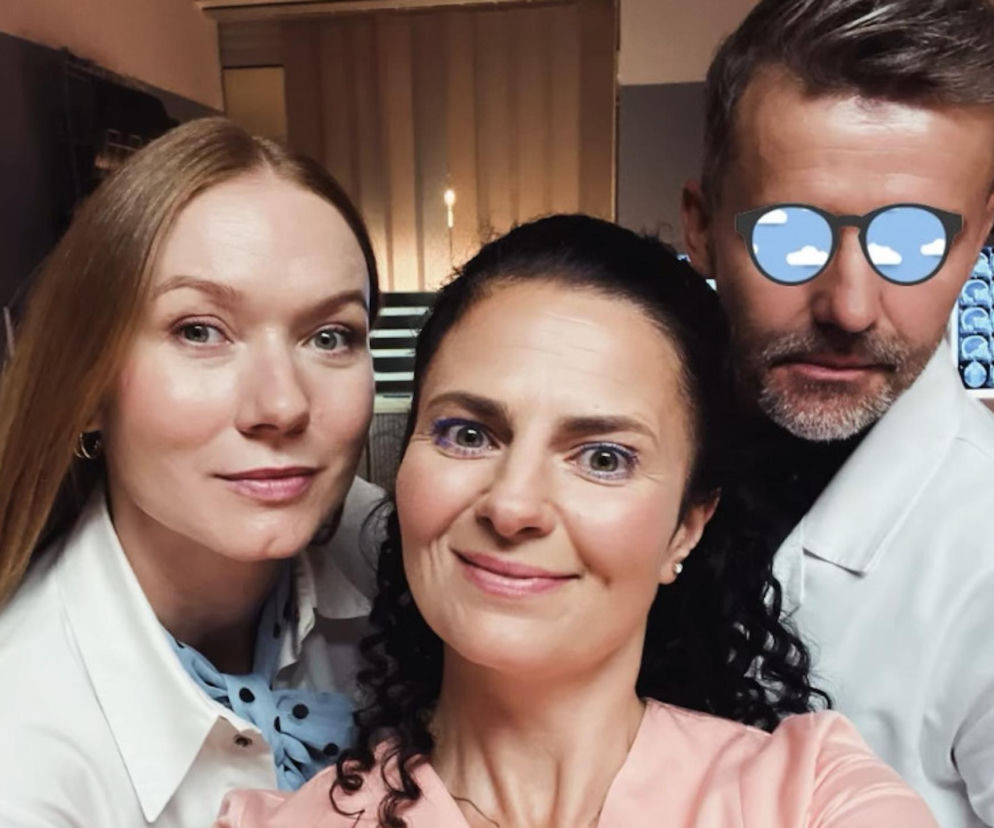 Katarzyna Dąbrowska jako Wiktoria Consalida z uśmiechem pozuje do selfie z dwiema innymi osobami, z czego jedna ma na twarzy okulary z niebieskimi chmurami. Na zdjęciu widać fragment pomieszczenia medycznego. Więcej o powrocie bohaterki Na dobre i na złe przeczytasz na Super Seriale.