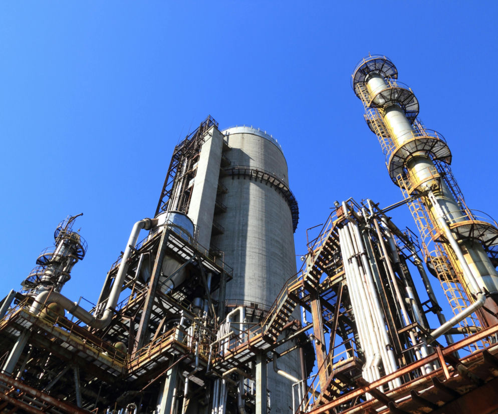 Rafineria ropy naftowej z wieżami destylacyjnymi i licznymi rurociągami, na tle czystego, błękitnego nieba. Infrastruktura symbolizuje globalny rynek paliw, o którym można przeczytać na portalu Super Biznes.