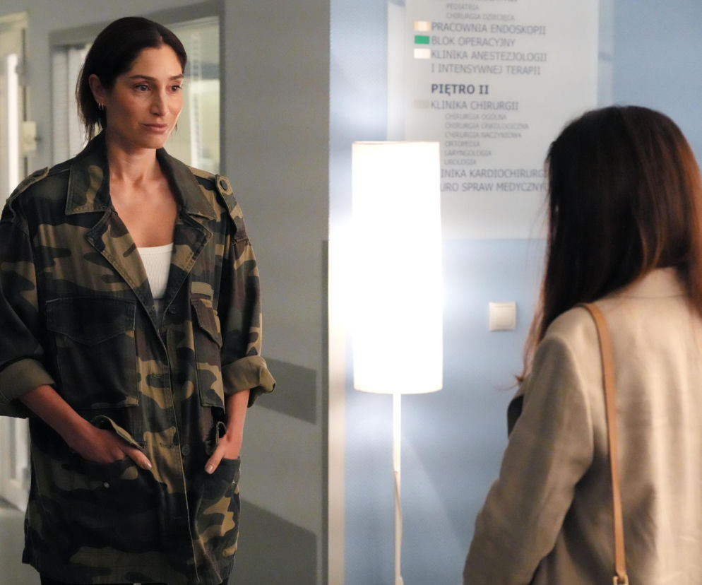 Celina (Orina Krajewska) w kurtce moro stoi w szpitalnym korytarzu, patrząc na plecy Kasi (Katarzyna Glinka). W tle widać tablicę informacyjną. Artykuł o odcinku 3315 Barw szczęścia przeczytasz na portalu Super Seriale.