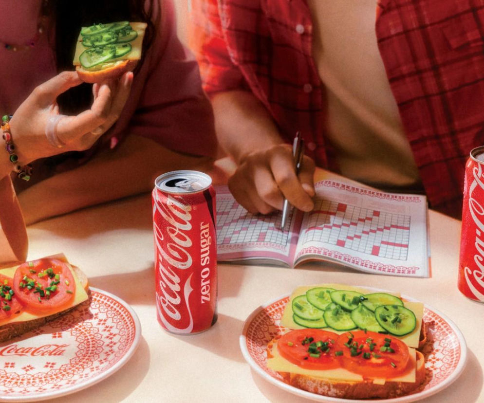 Dwie osoby przy stole z kanapkami na ceramice Bolesławiec i puszkami Coca-Cola. O loterii marek przeczytasz na SE.