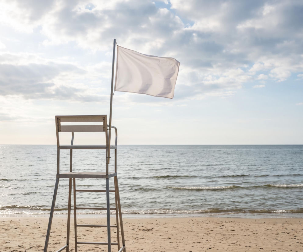 Biała flaga na wieży ratowniczej przy pustej plaży w Rewie. O warunkach kąpieli przeczytasz na Eska Trójmiasto.