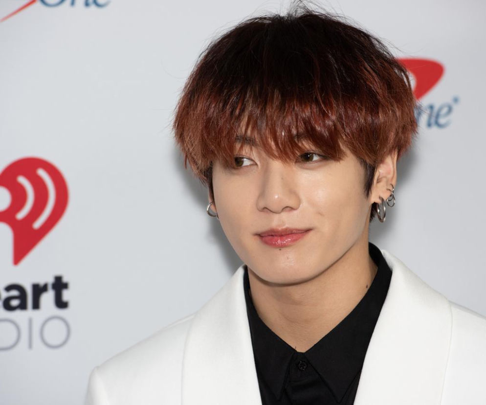 Jungkook z zespołu BTS w białej marynarce i czarnej koszuli, patrzący w bok. Ma brązowo-rudawą fryzurę i kolczyki. Fotografia nawiązuje do wyroku w sprawie stalkerki wokalisty, o czym przeczytasz więcej na naszym portalu.