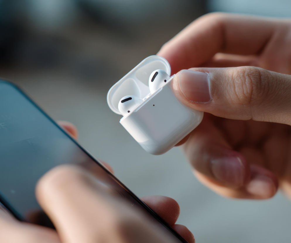 Dłonie osoby trzymającej smartfon i otwarte etui ze słuchawkami Apple AirPods Pro. O wyborze ANC przeczytasz na Eska.