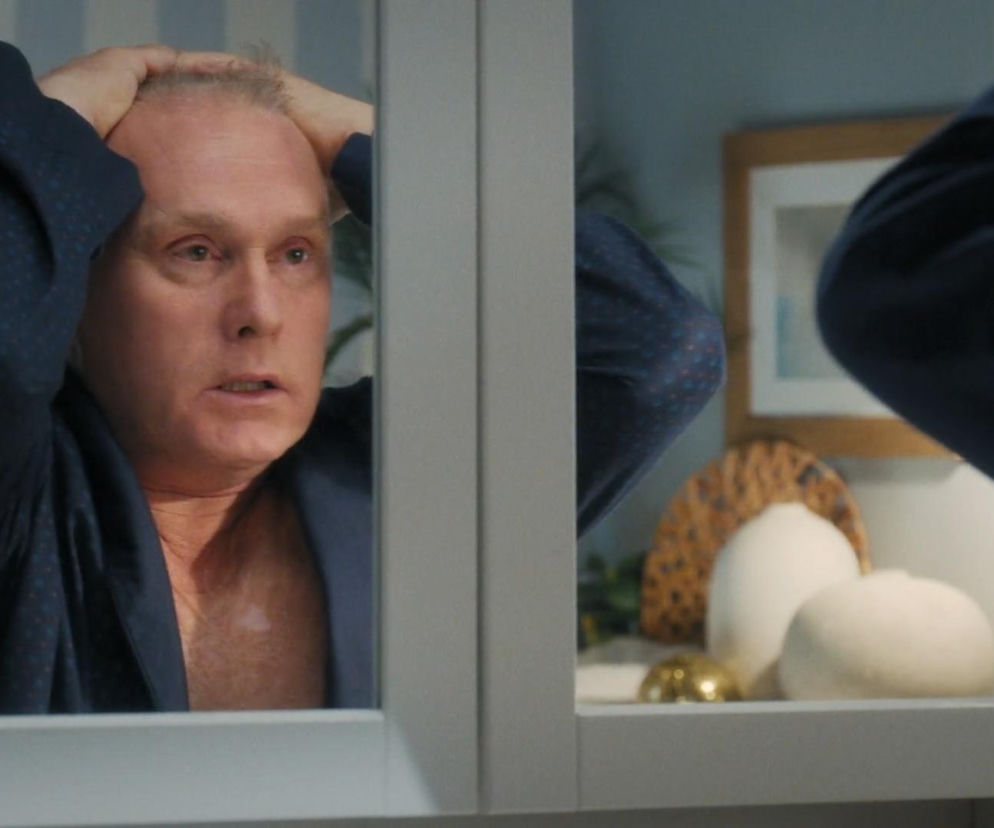 Robert Moskwa jako Artur Rogowski z M jak miłość w niebieskim szlafroku, patrzący w lustro z zmartwioną miną, trzymający dłonie na głowie, symbolizując jego rozdarcie między rodziną a uczuciami do Joanny. Więcej o losach bohatera przeczytasz na Super Seriale.