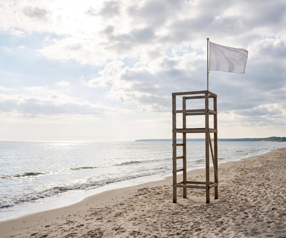 Drewniana wieża ratownicza z białą flagą na pustej plaży w Dąbkach. O bezpieczeństwie nad morzem czytaj w SE Szczecin.