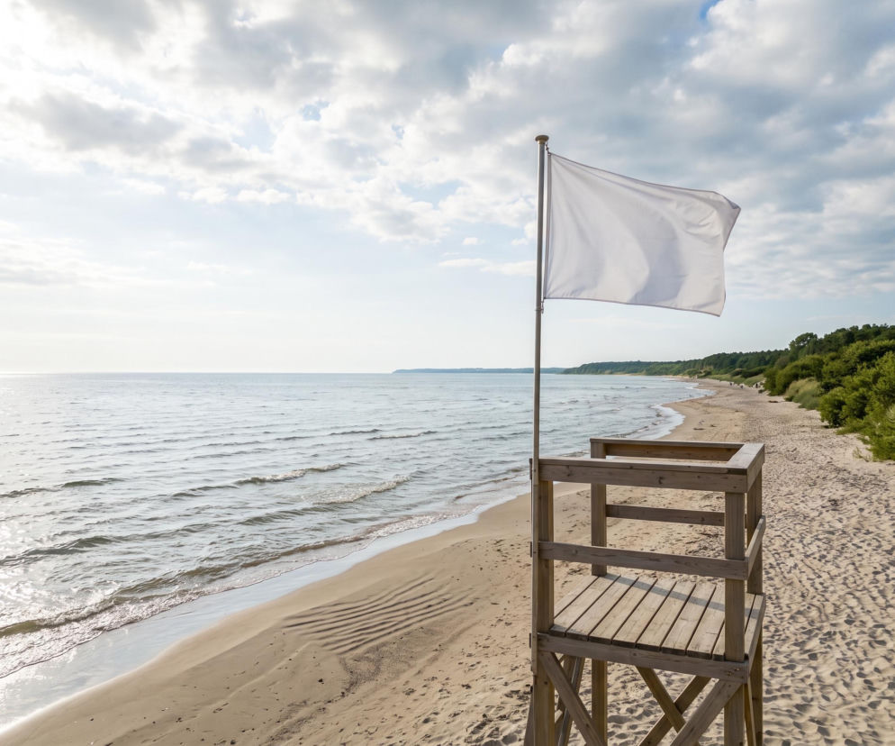Biała flaga na wieży ratowniczej przy pustej plaży. O bezpiecznych kąpieliskach w regionie przeczytasz na SE Szczecin.