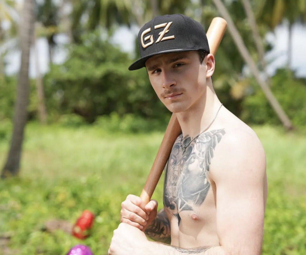 Szymon Królik z tatuażem na klatce piersiowej trzyma kij baseballowy. O nowym uczestniku Hotel Paradise przeczytasz w Eska.