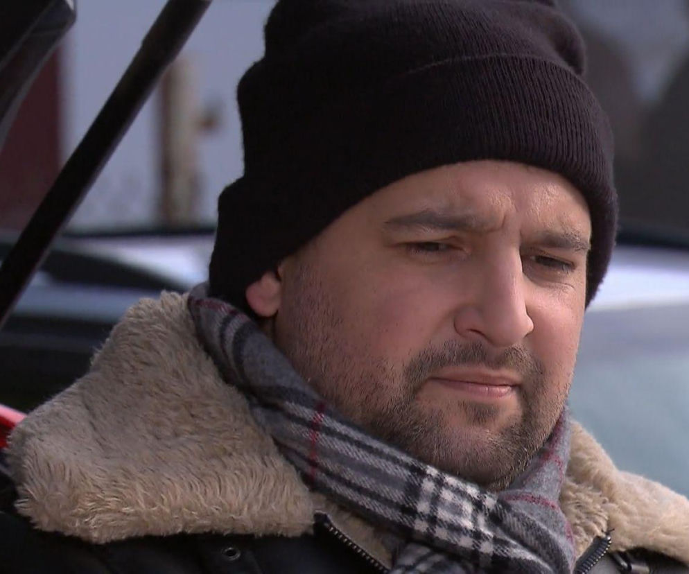 Mężczyzna w czarnej czapce i szaliku w kratę, ubrany w kurtkę z futrzanym kołnierzem, patrzy w dal z zamyśloną miną, na tle niewyraźnego otoczenia. Zbliżenie na jego twarz podkreśla kontekst emocjonalny serialu Klan i intrygujących wydarzeń, o których przeczytasz na Super Seriale.