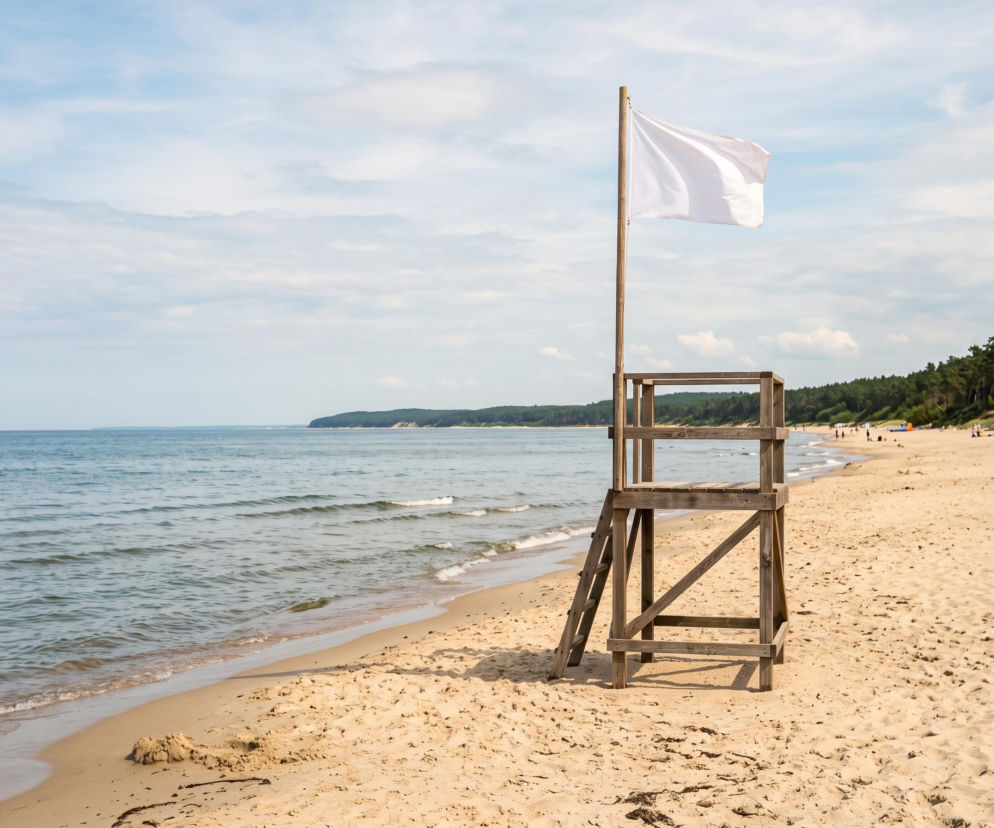 Drewniana wieżyczka ratownicza z białą flagą na piaszczystej plaży. O pogodzie w Krynicy Morskiej czytaj w Eska Trójmiasto.