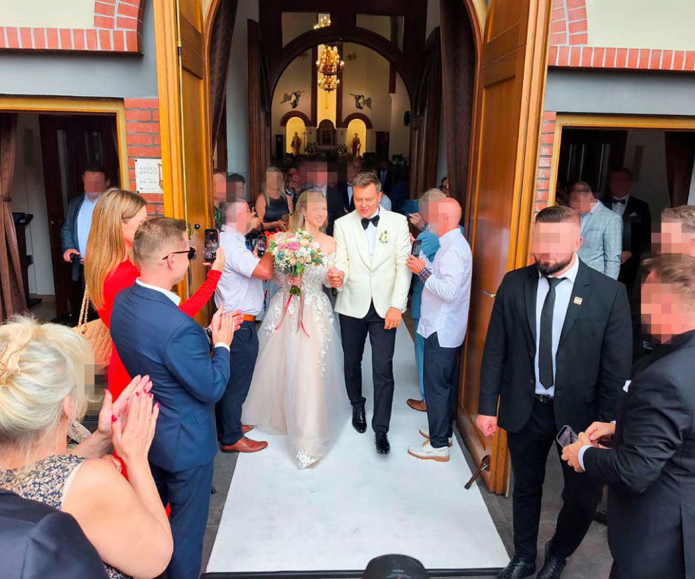 Rafał Brzozowski z żoną w różowej sukni wychodzą z kościoła wśród gości. O ślubie gwiazdora przeczytasz na SE.