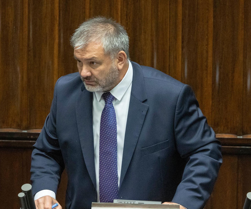 Mężczyzna w ciemnym garniturze i niebieskim krawacie stoi przy mównicy. O śledztwie prokuratora dowiesz się z Eska.