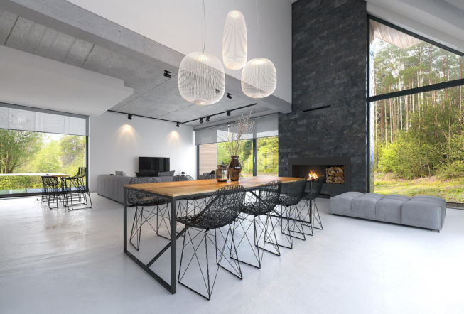 Nowoczesny salon w stylu industrialnym z betonowym sufitem, kamiennym kominkiem i widokiem na las