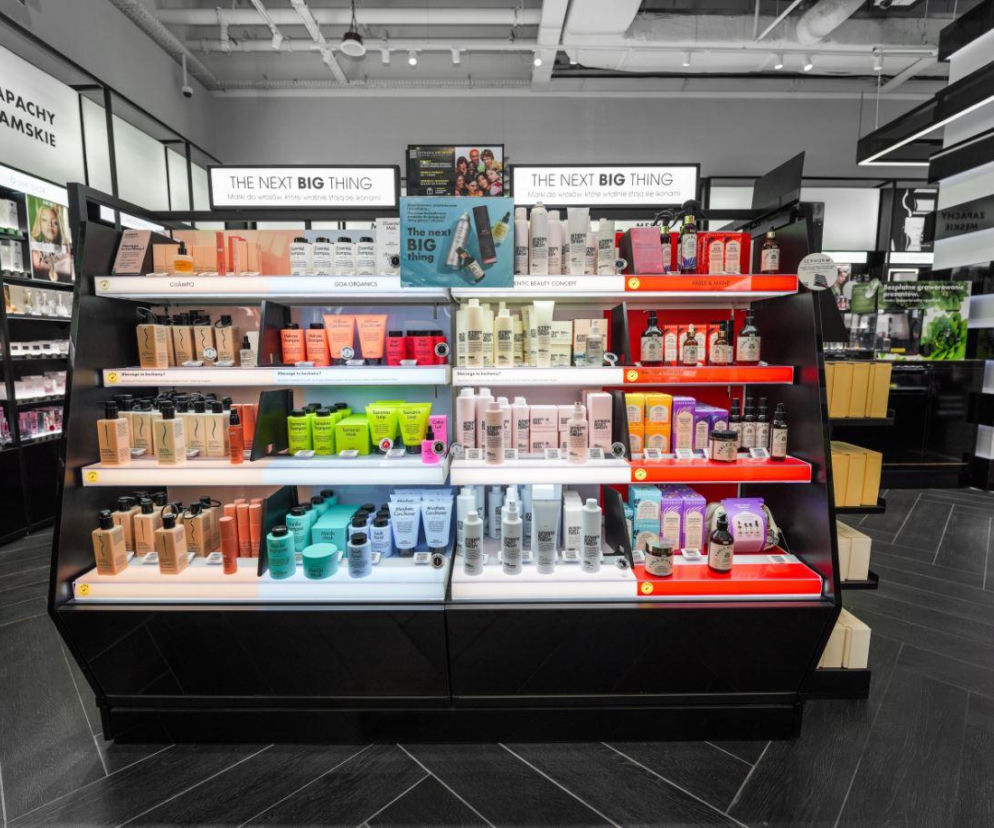 Wnętrze perfumerii Sephora z regałem prezentującym kosmetyki do włosów marek takich jak Cha.mpu, Goa Organics, Authentic Beauty Concept. Na górze regału widoczne ekrany z napisem The Next Big Thing, promujące nowe trendy w pielęgnacji. Po lewej stronie widać półki z zapachami damskimi, a po prawej dalszą część sklepu. O innowacjach w świecie urody możesz przeczytać na naszym portalu.