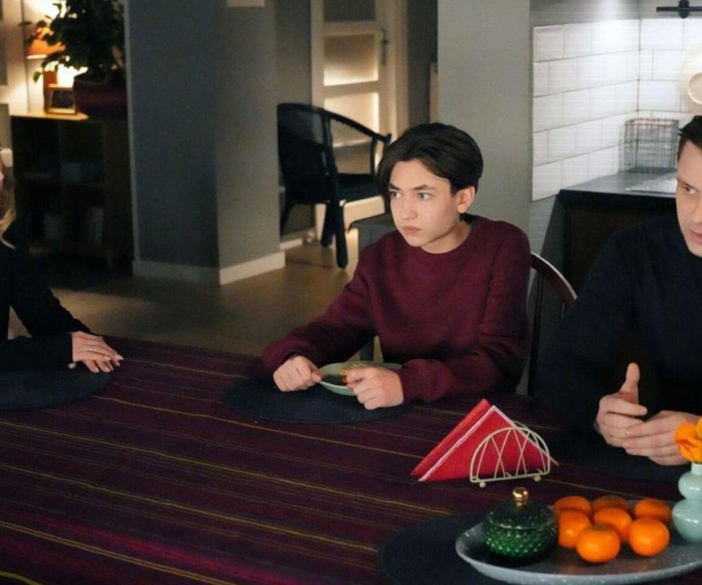 Asia (Anna Gzyra-Augustynowicz) z synem Emilem (Artem Malaszczuk) i Hubertem (Marek Molak) siedzą przy stole. Asia i Hubert mają poważne miny, a Emil patrzy w bok. Na stole talerz z mandarynkami i serwetnik. Więcej o ich losach w Barwach szczęścia na Super Seriale.