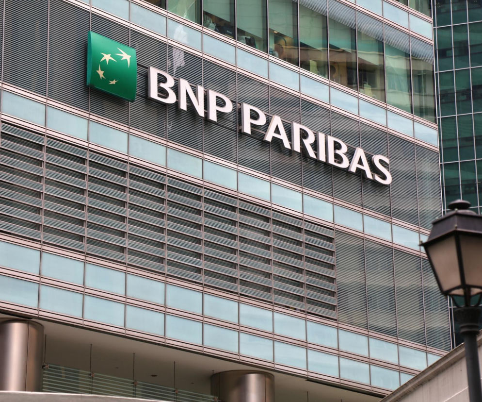 Budynek BNP Paribas z logo banku na szklanej fasadzie, w tle fragment drugiego biurowca i latarnia uliczna. Widok idealnie ilustruje temat redukcji etatów w banku. Więcej na ten temat przeczytasz na portalu Super Biznes.