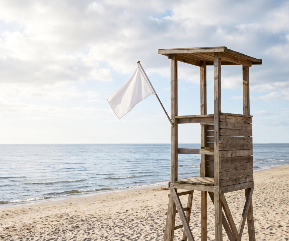 Drewniana wieża ratownicza z białą flagą na pustej plaży w Sarbinowie. O bezpieczeństwie nad wodą przeczytasz w SE Szczecin.