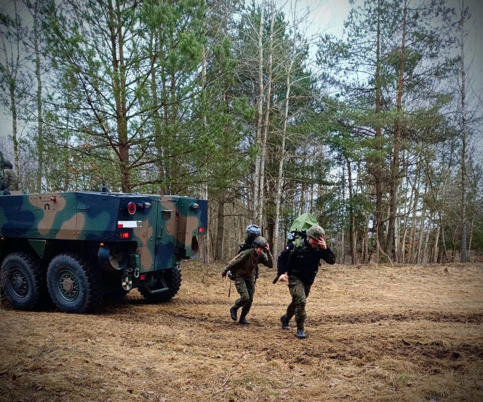 Polscy żołnierze w pełnym umundurowaniu z plecakami maszerujący obok wojskowego pojazdu opancerzonego typu Rosomak w lesie. Ilustruje to kontekst zmian w systemie emerytalnym mundurowych i drugą emeryturę z ZUS, o czym przeczytasz na Super Biznes.