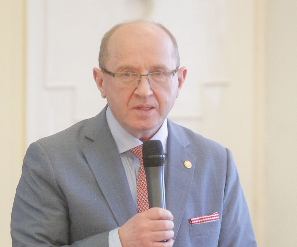 Prof. dr n. med. dr h.c. multi Henryk Skarżyński w jasnym garniturze, krawacie w czerwono-białe wzory i okularach, trzymający mikrofon. To prezes CI2026, o czym przeczytasz więcej na Super Biznes.