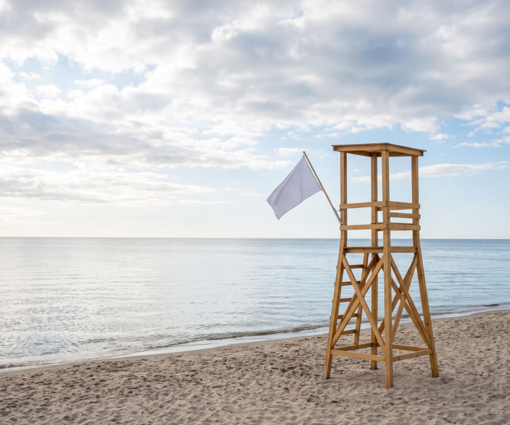 Drewniana wieża ratownicza z białą flagą na pustej plaży. O bezpieczeństwie kąpieli w Dziwnowie przeczytasz na SE Szczecin.