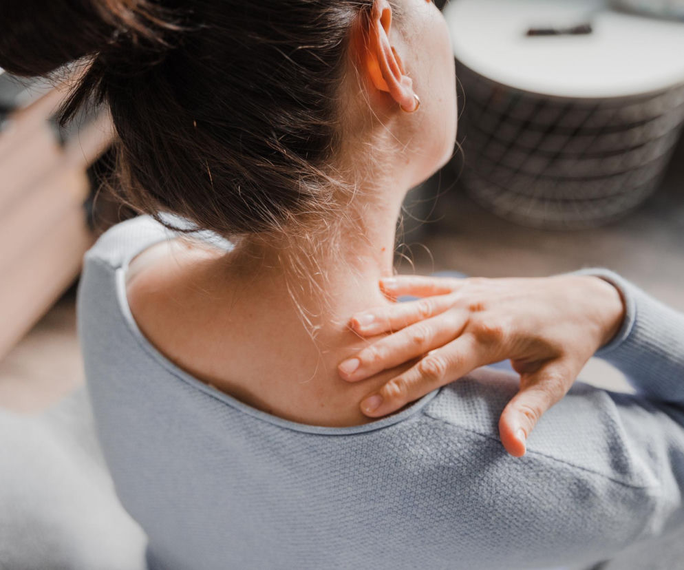 Kobieta dotyka bolącego karku i ramienia, symbolizując napięcie mięśniowe i fizyczne objawy stresu. Więcej o tym, jak rozpoznać i wyciszyć takie sygnały, znajdziesz na Poradnik Zdrowie.