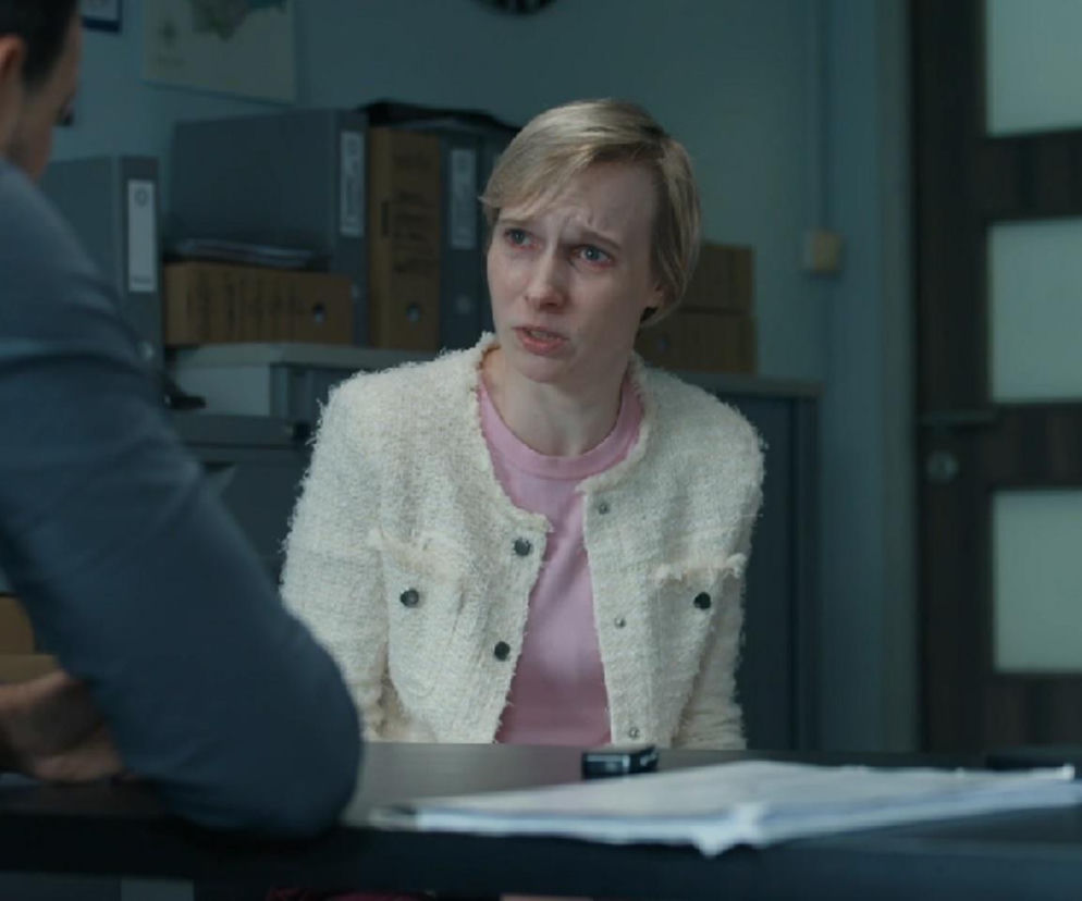 Sonia (Weronika Nockowska) w jasnym, teksturowym żakiecie i różowej bluzce, z krótkimi blond włosami i zapłakaną twarzą, składa zeznania Kodurowi (Oskar Stoczyński) w pomieszczeniu przypominającym komisariat, w tle stoi kobieta w policyjnym mundurze. Więcej o dramatycznym przesłuchaniu w Barwy szczęścia na stronie Super Seriale.