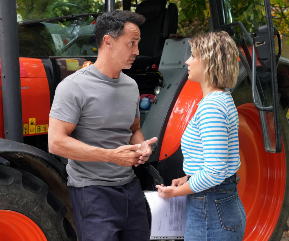 Mariusz (Rafał Cieszyński) i Janka (Oliwia Drożdżyk) rozmawiają, stojąc przy czerwonym traktorze. Janka trzyma dokumenty i jest zaskoczona jego słowami w nowym odcinku Barw szczęścia. Więcej o tym na Super Seriale.