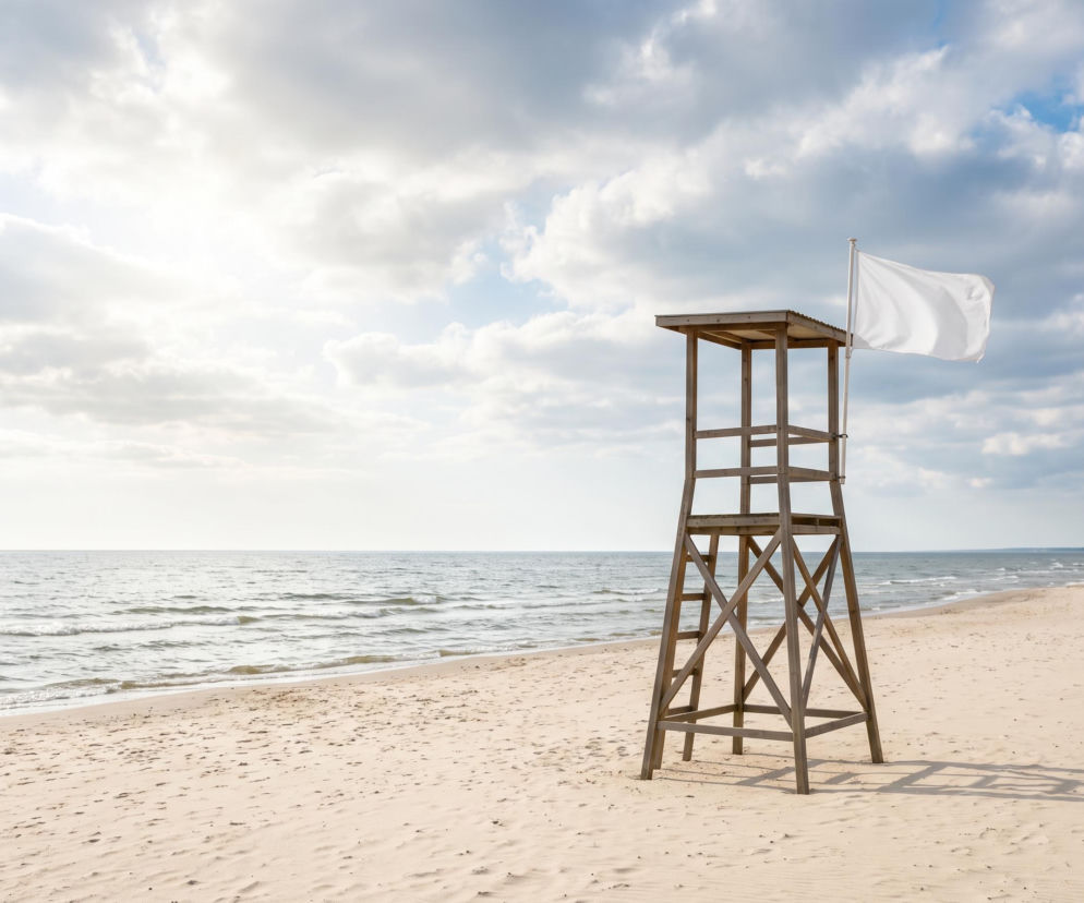 Drewniana wieża ratownika z białą flagą na pustej plaży. O bezpiecznych kąpielach w Mielnie przeczytasz na SE Szczecin.