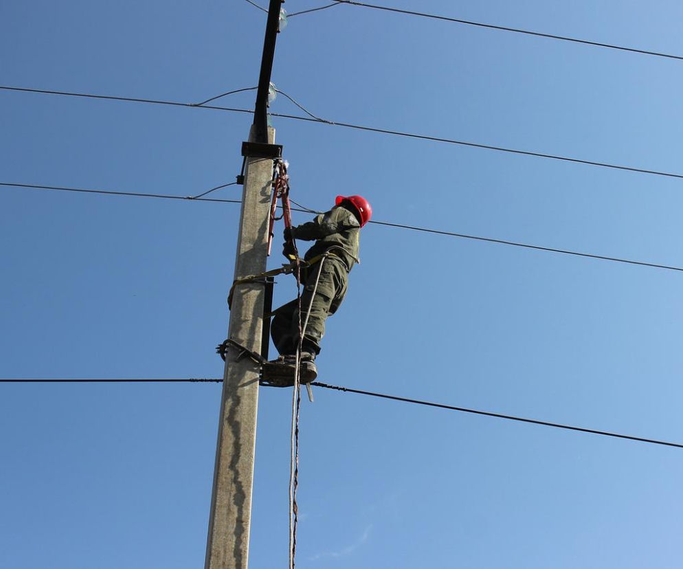 Elektryk w kasku naprawia linię na słupie. O wielkiej awarii prądu pod Warszawą przeczytasz na SE.