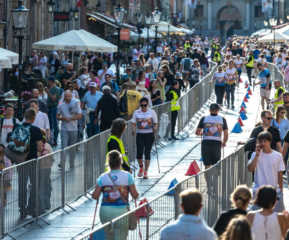 Uczestnicy Biegu po Nowe Życie maszerujący z kijkami nordic walking po specjalnie wytyczonej trasie wzdłuż ulicy Długiej w Gdańsku, otoczeni tłumem kibiców i spacerowiczów. Wydarzenie promuje świadome dawstwo narządów i edukuje o transplantacji, o czym więcej można przeczytać na portalu Poradnik Zdrowie.