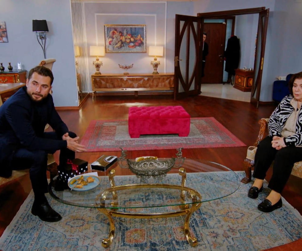 Kuzey i Naciye siedzą w salonie. Kuzey ubrany w granatową marynarkę i spodnie, z brodą, siedzi na beżowym fotelu, patrząc na matkę. Naciye w bluzce w zebrę, ciemnych spodniach, siedzi naprzeciwko syna. Pomiędzy nimi szklany stolik kawowy. Więcej o Miłości i nadziei na Super Seriale.