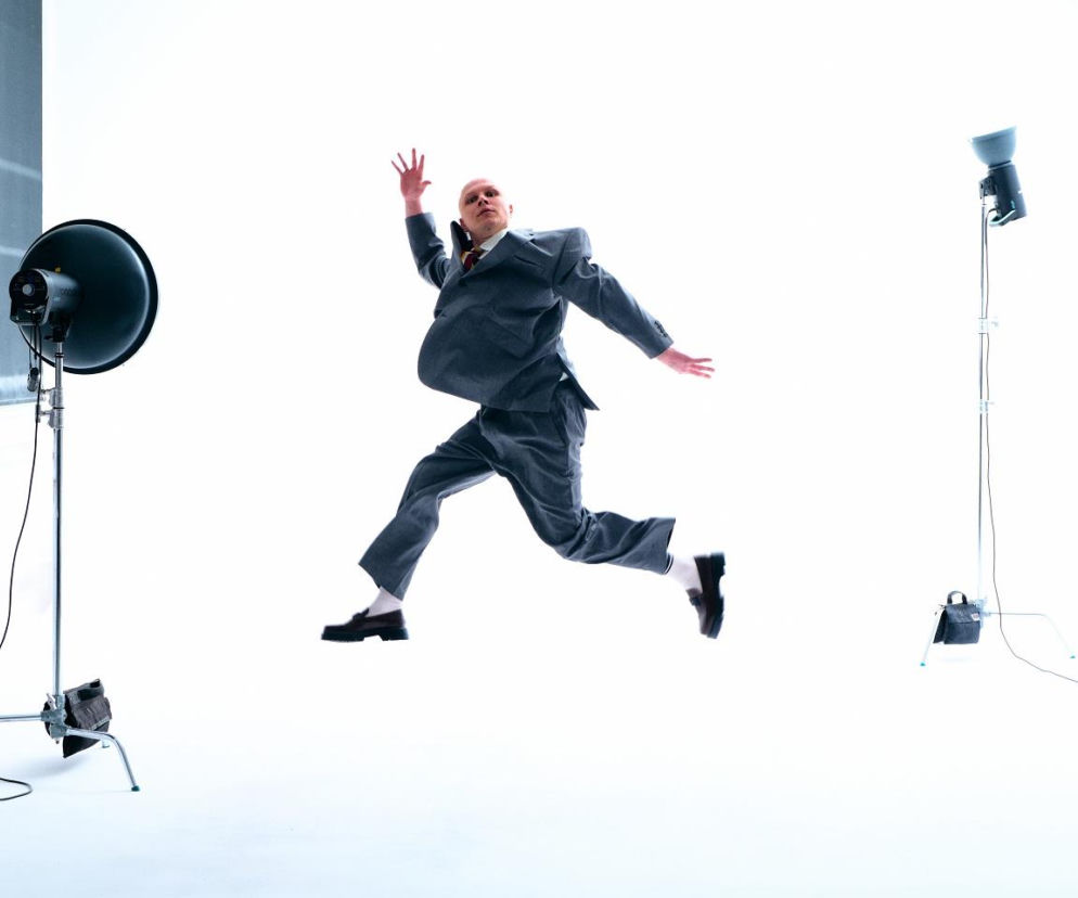 Muzyk Jędrzej Wise w szarym garniturze skacze w studiu fotograficznym. O nowym singlu artysty przeczytasz na EskaRock.