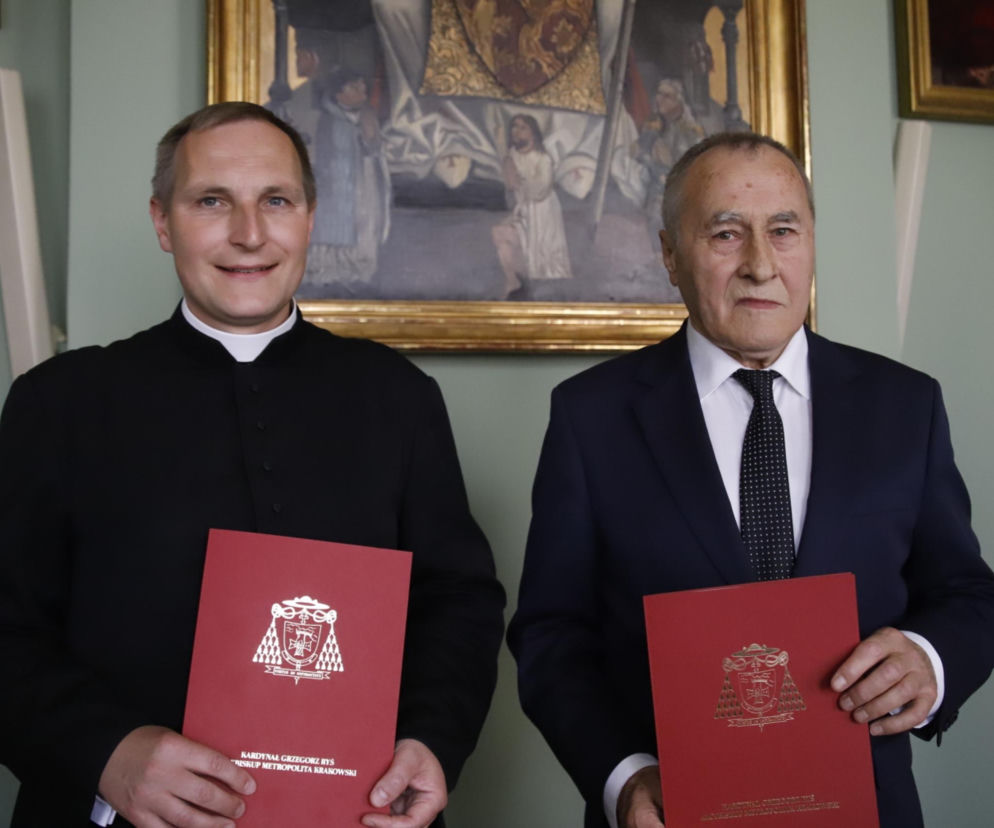 Ksiądz Rafał Buzała i Lucjan Tabaka, nowy ekonom Archidiecezji Krakowskiej, prezentują akty nominacji. W tle widoczny obraz religijny, tworzący formalną atmosferę. Więcej o zmianach w zarządzaniu archidiecezją przeczytasz na naszym portalu.