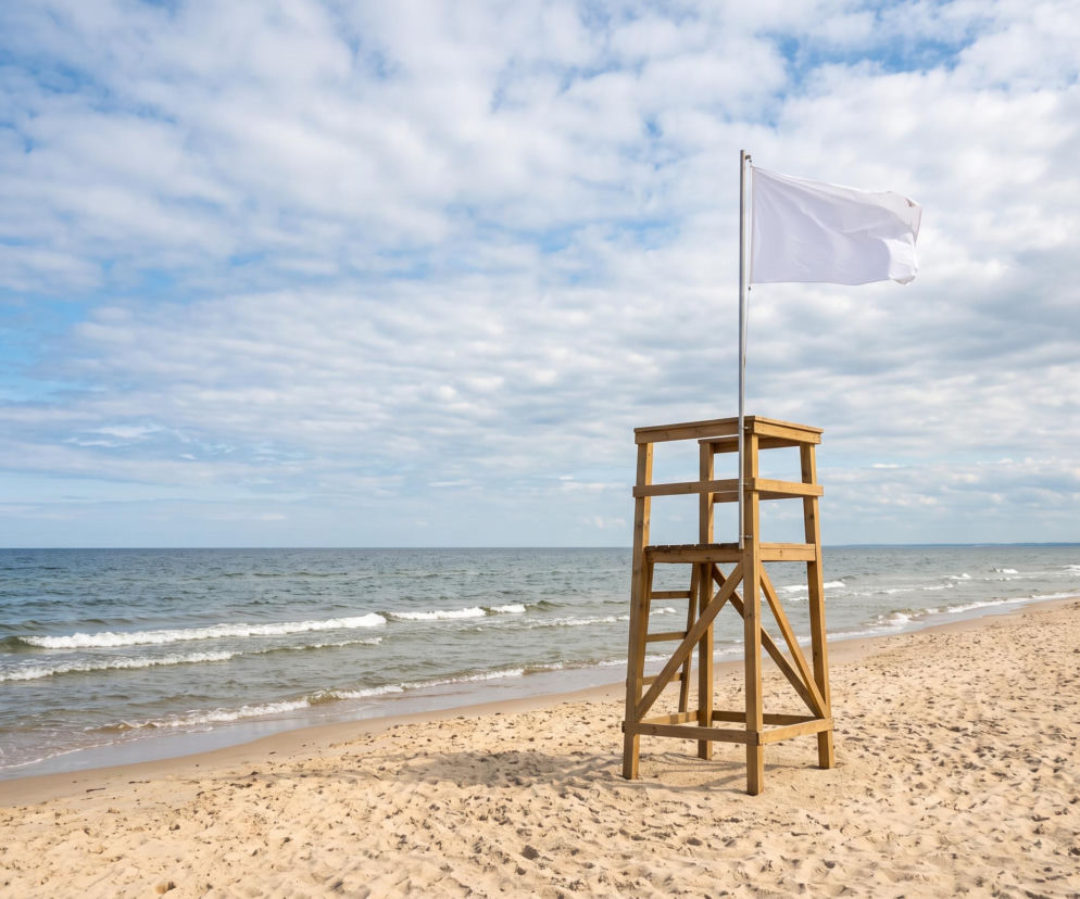 Drewniana wieża ratownika z białą flagą na plaży w Ustroniu Morskim. O bezpieczeństwie nad wodą przeczytasz na SE Szczecin.