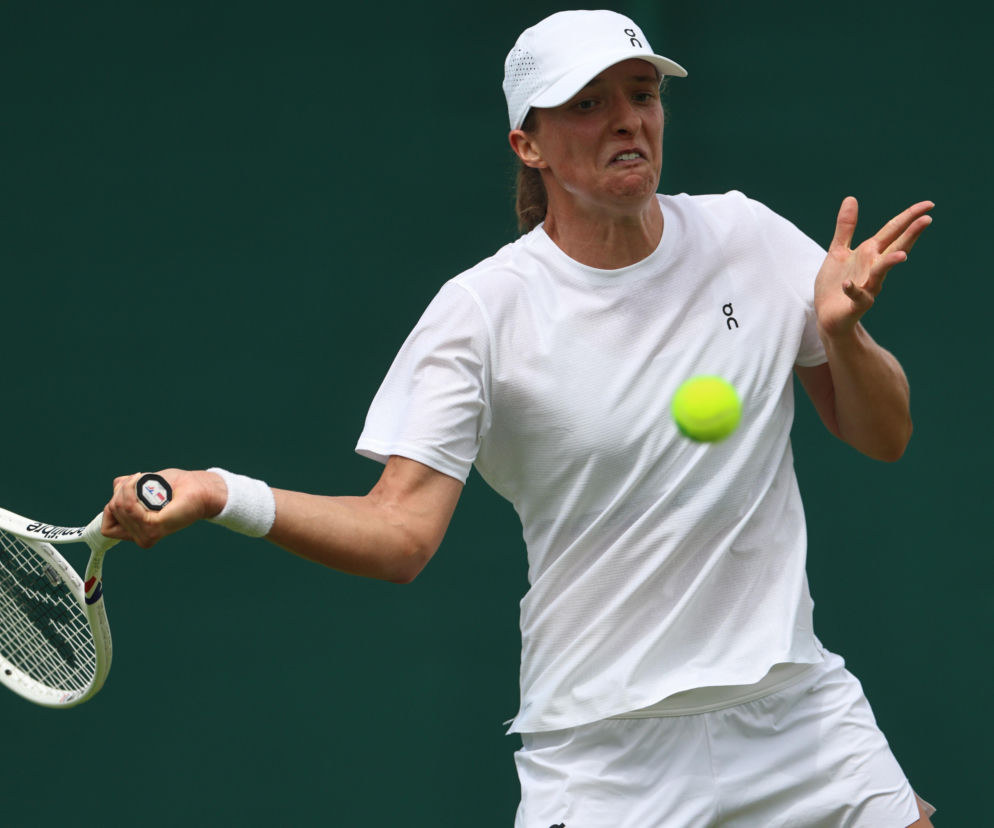 Iga Świątek w akcji na korcie tenisowym Wimbledonu, dynamicznie uderza piłkę, prezentując skupienie i determinację. Tenisistka ma na sobie białą koszulkę, spodenki oraz czapkę z daszkiem. Na naszym portalu znajdziesz więcej informacji o turnieju i nagrodach.