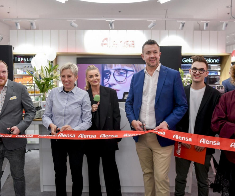 Grupa pięciu osób przecina czerwoną wstęgę z logo Alensa podczas uroczystego otwarcia nowego salonu optycznego w Warszawie. Na środku Edyta Folwarska z mikrofonem. Więcej o wydarzeniu i planach firmy przeczytasz na Super Biznes.