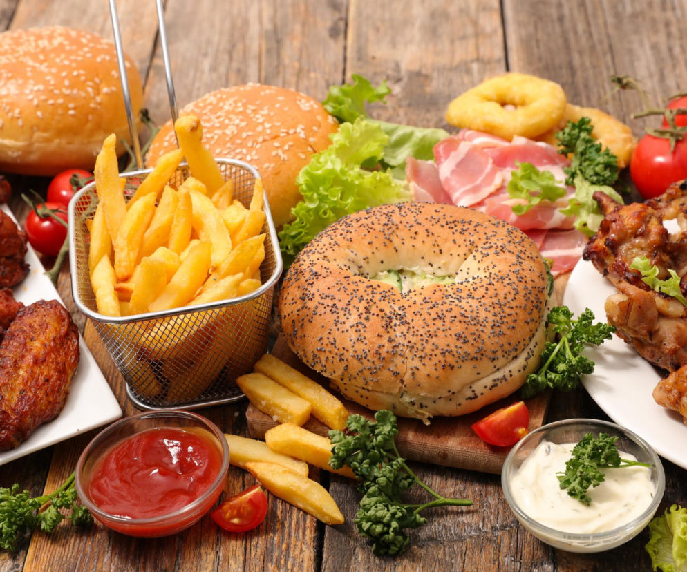 Zestaw żywności ultraprzetworzonej: frytki, burgery, smażony kurczak i bekon. O wpływie takiej diety na mózg przeczytasz w PZ Fit.