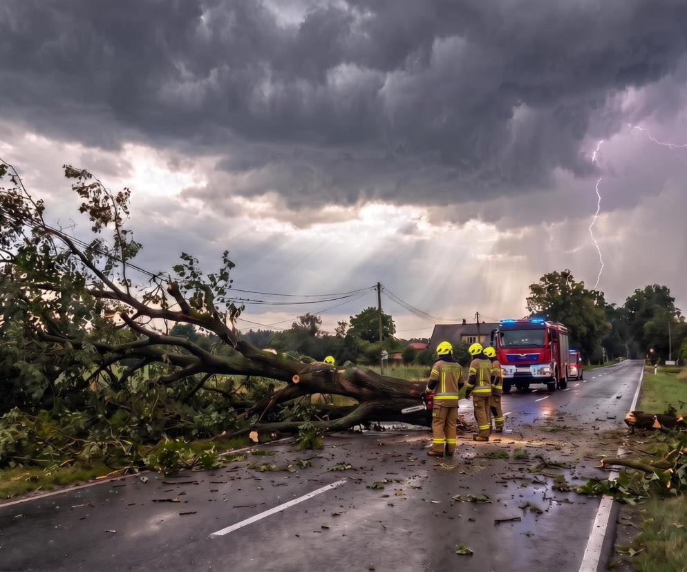 Strażacy przy powalonym drzewie na drodze pod burzowym niebem z piorunem. O skutkach nawałnic przeczytasz w Eska.