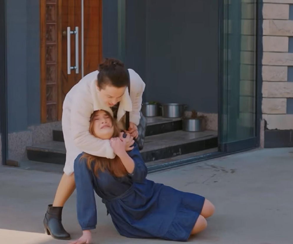 Kobieta w białym płaszczu dusi drugą, leżącą na ziemi, ubraną w granatową sukienkę, w dramatycznej scenie z serialu Miłość i nadzieja. Emocje są intensywne, oddając brutalny atak Cavidan na Silę. Więcej o tych mrożących krew w żyłach wydarzeniach przeczytasz na Super Seriale.