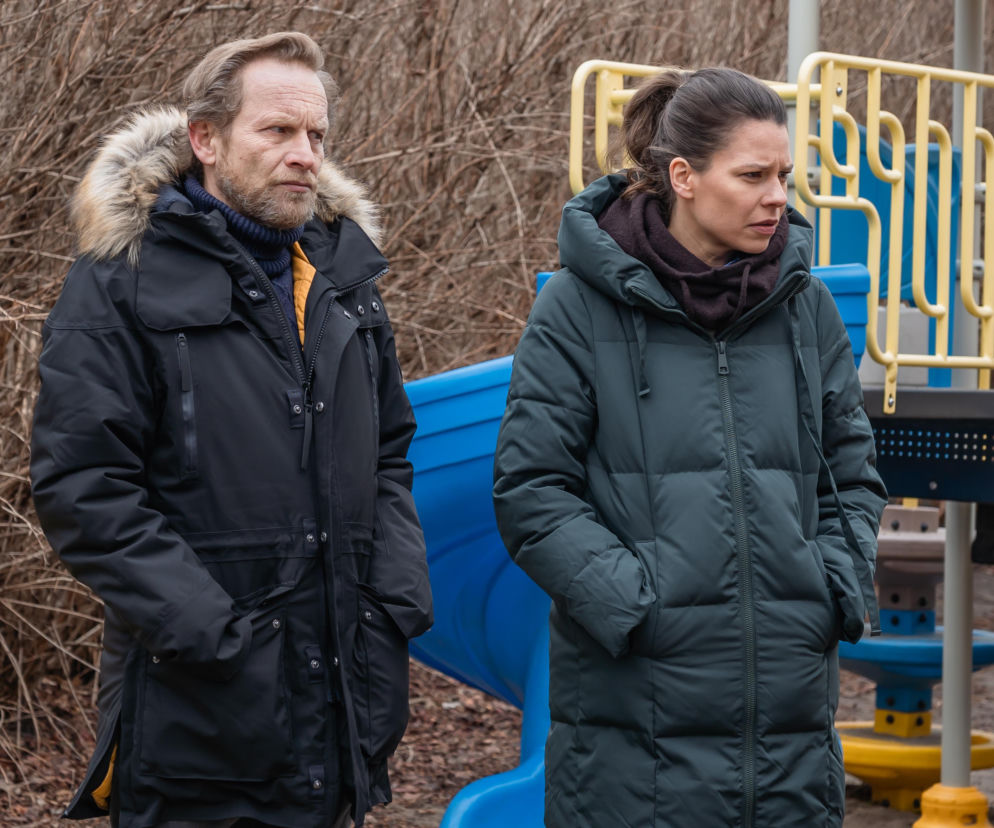 Artur Dziurman jako Roman Musashi Gołaszewski w czarnej kurtce z futrzanym kapturem i Aleksandra Gałczyńska jako Alicja Lipiec w zielonej puchowej kurtce, stojący na placu zabaw, to kadr z serialu Sprawiedliwi. Trójmiasto. Więcej o serialu na Super Seriale.