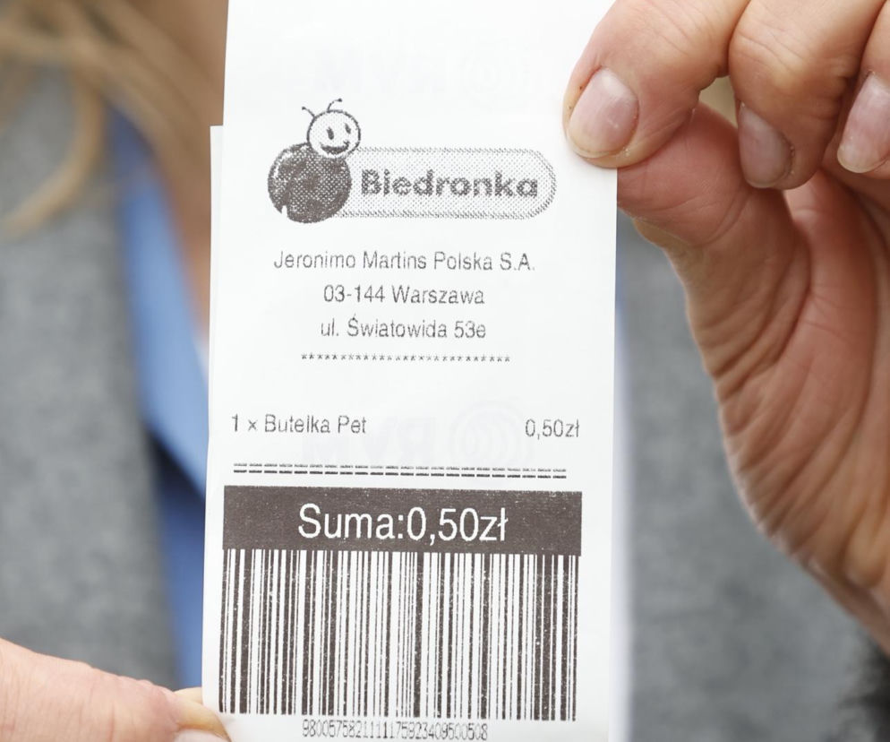 Dłonie osoby trzymającej wydruk z automatu na butelki o wartości 50 groszy. O systemie kaucyjnym przeczytasz na SE Superbiz.