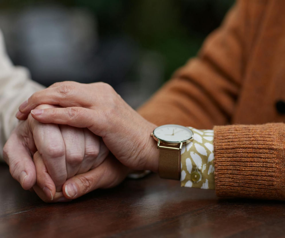 Dwie osoby trzymające się za ręce w geście wsparcia i opieki, co doskonale ilustruje troskę o bliskich z chorobą Alzheimera. Możesz przeczytać więcej o opiece nad starszymi na portalu Poradnik Zdrowie.